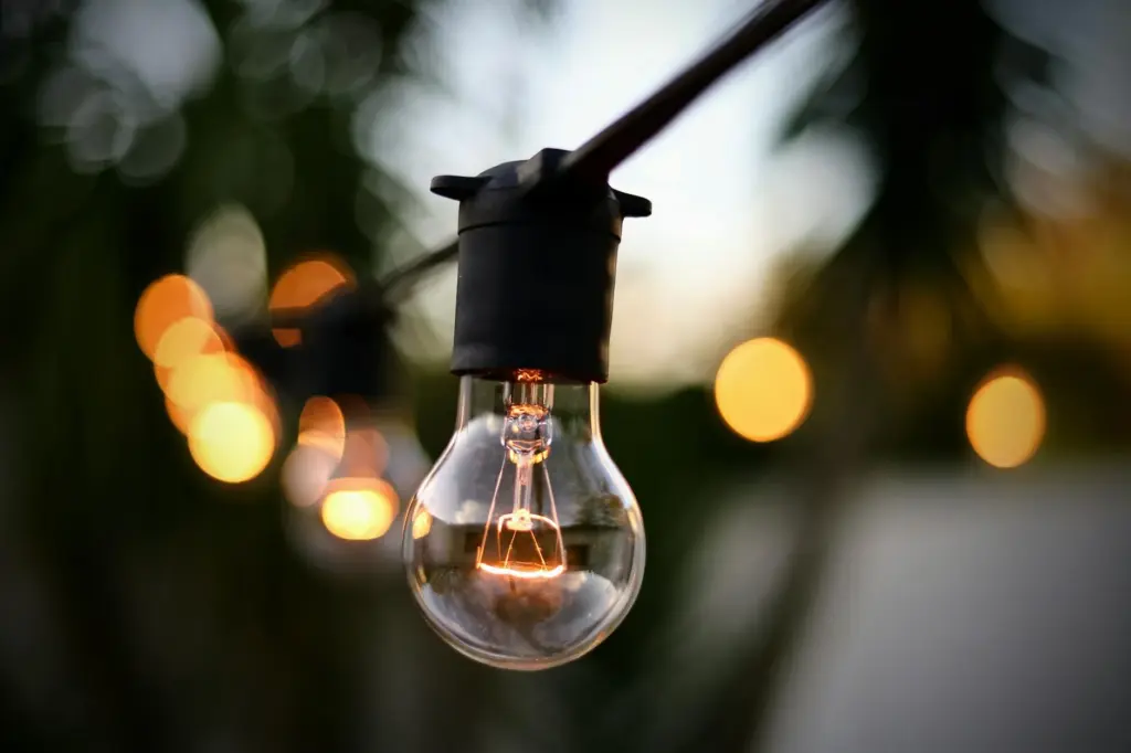 Illuminated light bulb hanging on string with bokeh backdrop outdoors.