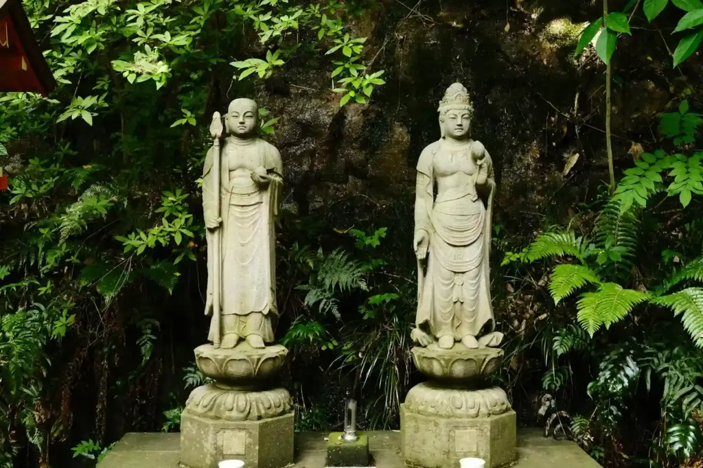 Two serene Buddhist statues surrounded by lush greenery in a tranquil Tokyo garden.
