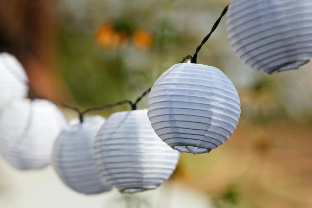 A row of white paper lanterns hanging on a wire outdoors with soft, natural sunlight.
