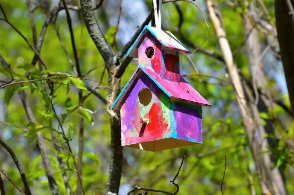 Vibrant painted birdhouse hanging among green leaves in Collingwood, Canada.