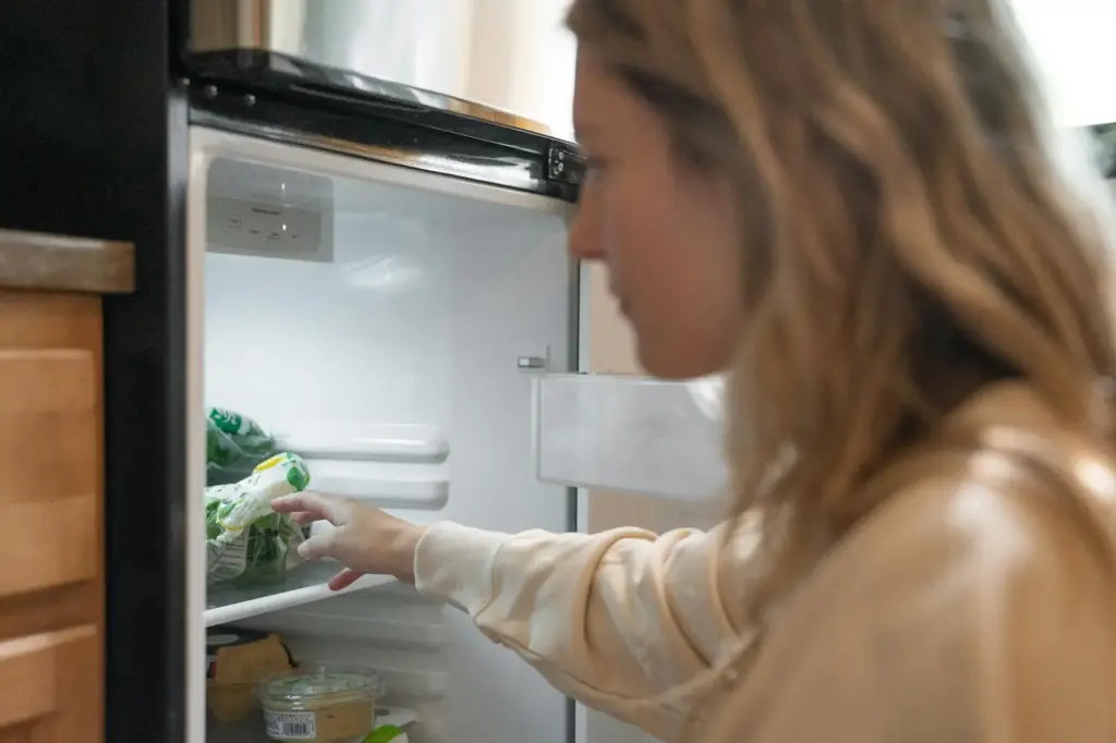 Woman grabbing vegetables from a refrigerator, symbolizing healthy living.