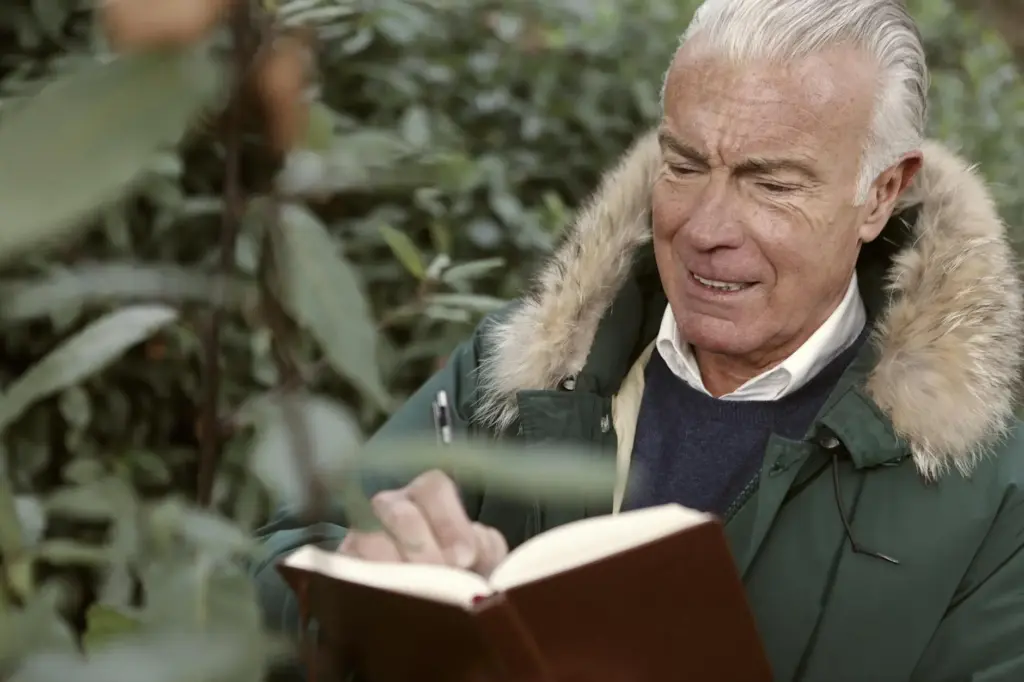 Senior man in a fur-lined coat writing in a notebook outdoors.