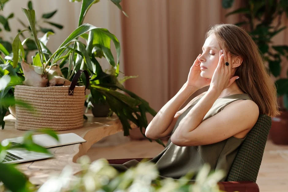 A woman relaxes, massaging her temples among indoor plants in a bright, sunlit room.