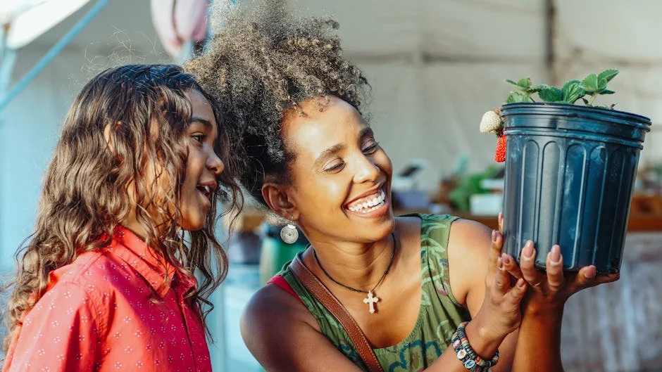 Mother and daughter smiling and holding a strawberry plant, showcasing happiness and togetherness.