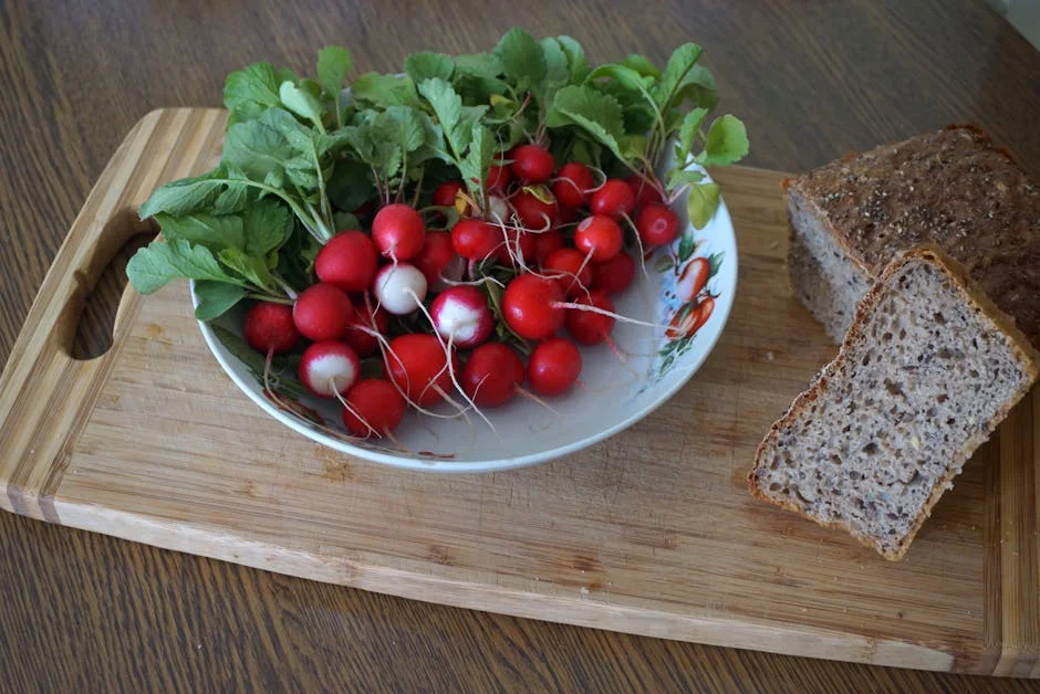 A vibrant display of radishes with leafy greens and whole grain bread on a wooden cutting board.