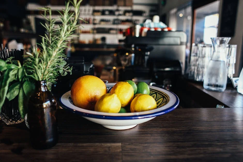A colorful mix of lemons, limes, and oranges in a bowl on a kitchen worktop with rosemary and basil.