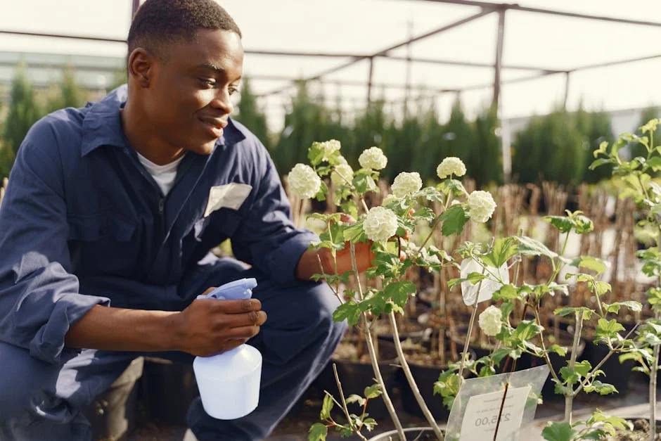 Smiling young gardener watering plants in a nursery garden with a spray bottle.