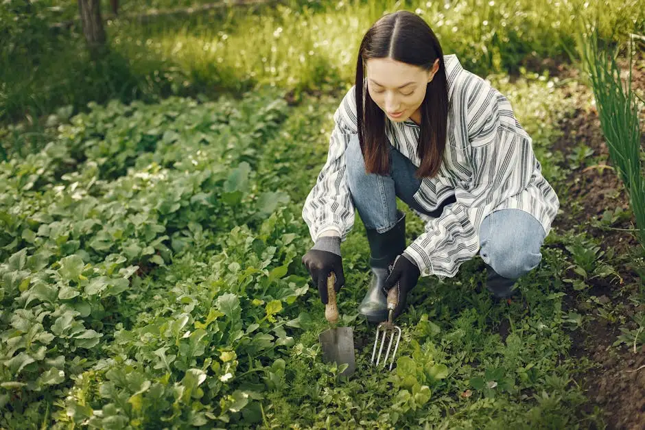 A young woman tends to her garden, cultivating vibrant greens with garden tools on a sunny day.