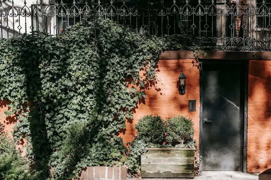 Elegant brick wall with lush ivy and plants, showcasing a stylish black door and ornate balcony railing.