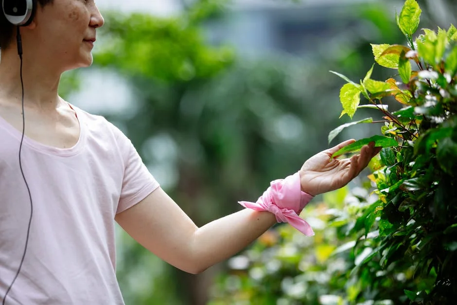 A woman in a pink t-shirt and headphones touching green leaves in a park, capturing a serene connection with nature.