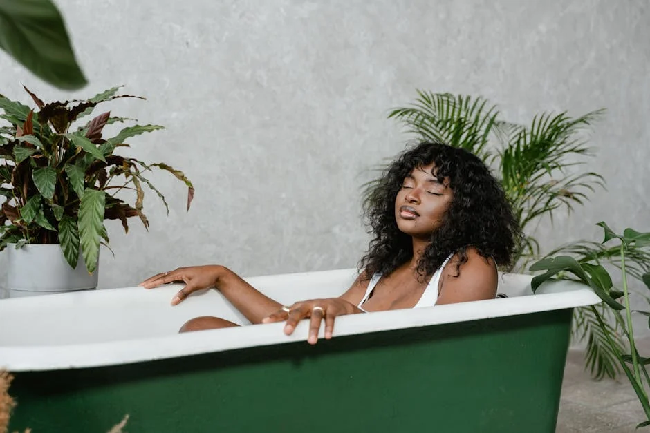 A serene woman with eyes closed, relaxing in a green bathtub surrounded by decorative plants.