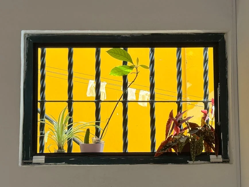 Houseplants adorn a windowsill with a vibrant yellow outdoor backdrop, adding a lively touch.