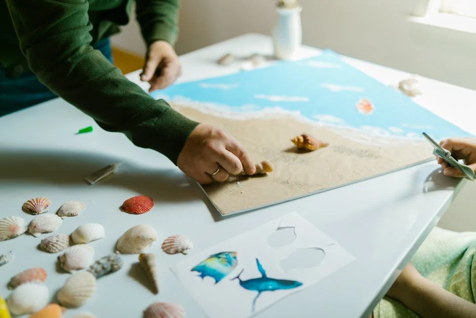 Hands working on a seashell artwork on a table with scattered seashells and other art materials.