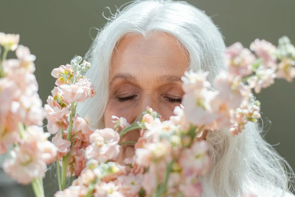 Elderly woman enjoying delicate pink blossoms, eyes closed in tranquility.