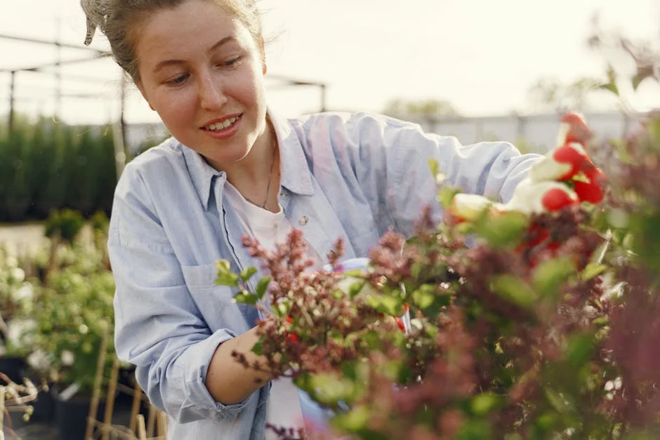 A smiling woman tends to colorful flowers in an outdoor garden during the day.