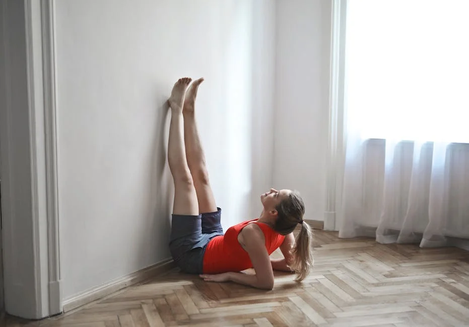 A woman in a red top performs a yoga stretch with legs vertical against a wall.