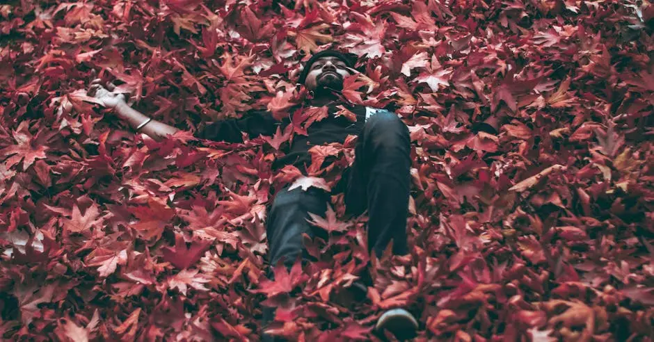 Man lying peacefully in a bed of vibrant red maple leaves during fall.