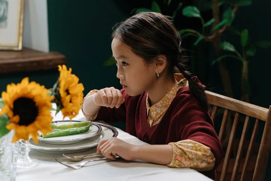 A young girl in a red sweater sits at a table decorated with sunflowers, poised with cutlery.