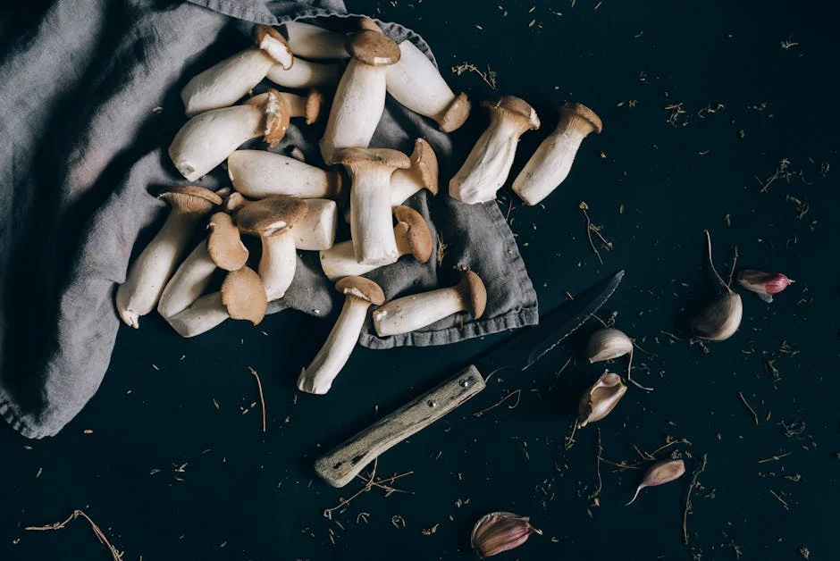 Fresh king oyster mushrooms on a dark surface with a knife and garlic, ready for cooking.