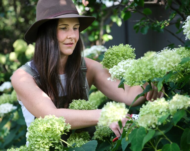 A woman in a hat picking flowers from a bush