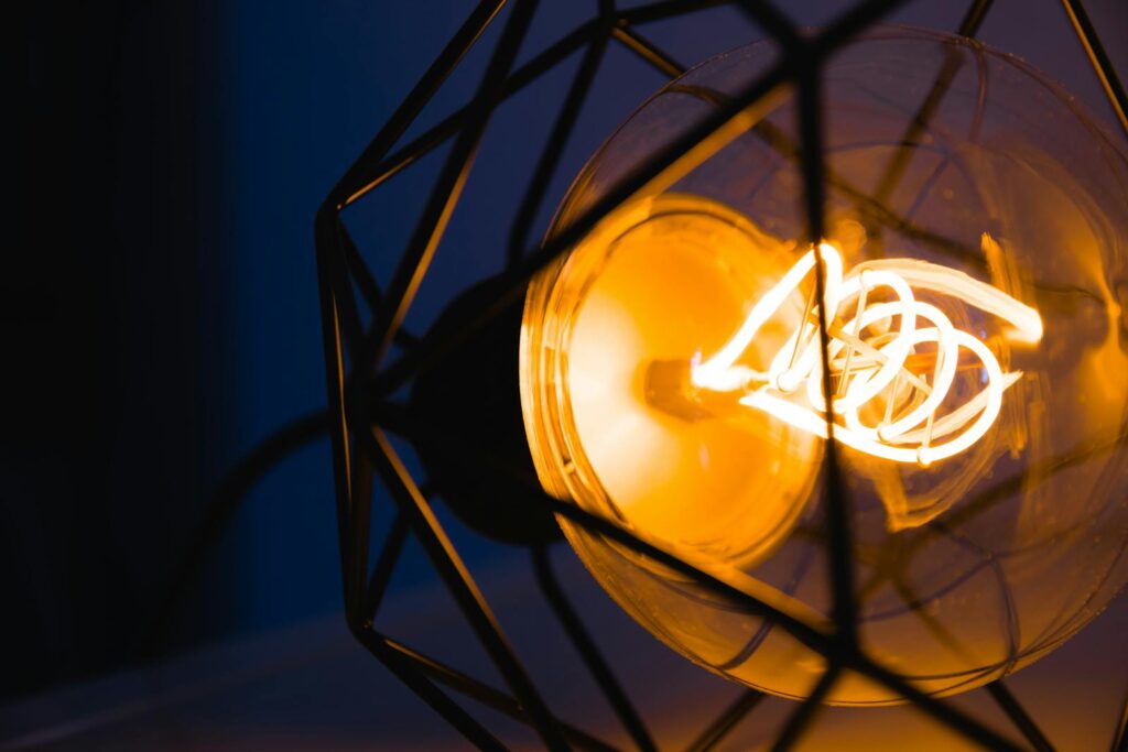 A glowing light bulb captured in a metal geometric frame, illuminating its surroundings.