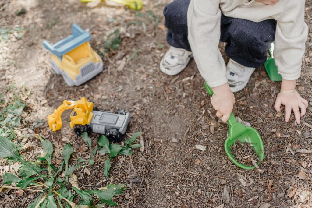 High angle of unrecognizable child playing with plastic toys sitting on ground in yard