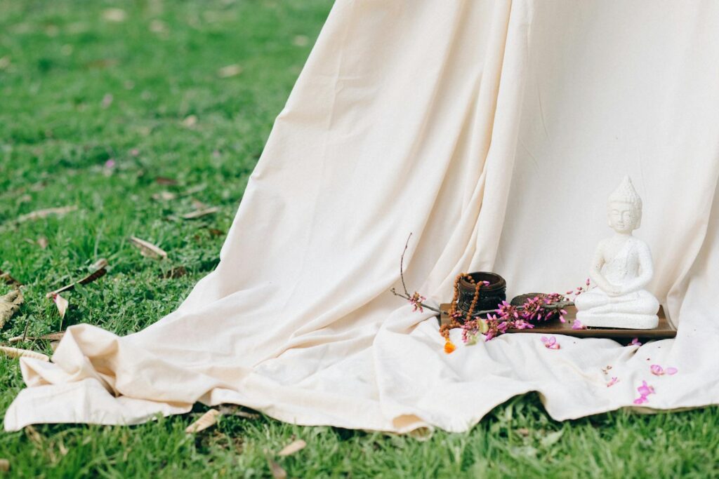 A serene Buddha statue with colorful blossoms and fabric drapery in a tranquil outdoor setting.