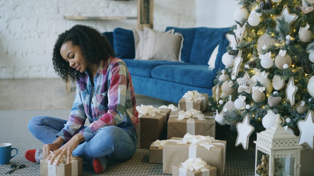 Young woman wrapping christmas presents near decorated tree.