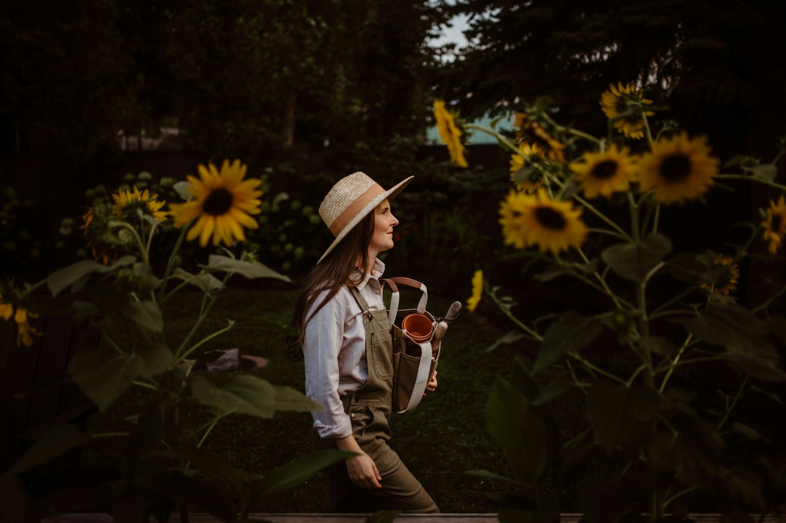 A woman wearing a hat and vest standing in a field of sunflowers