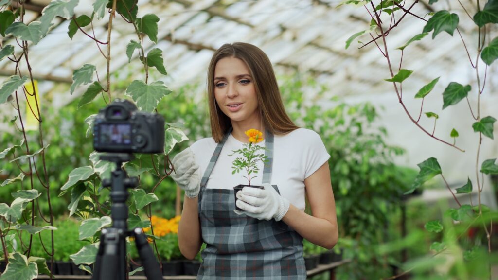 Woman filming herself with flower in greenhouse