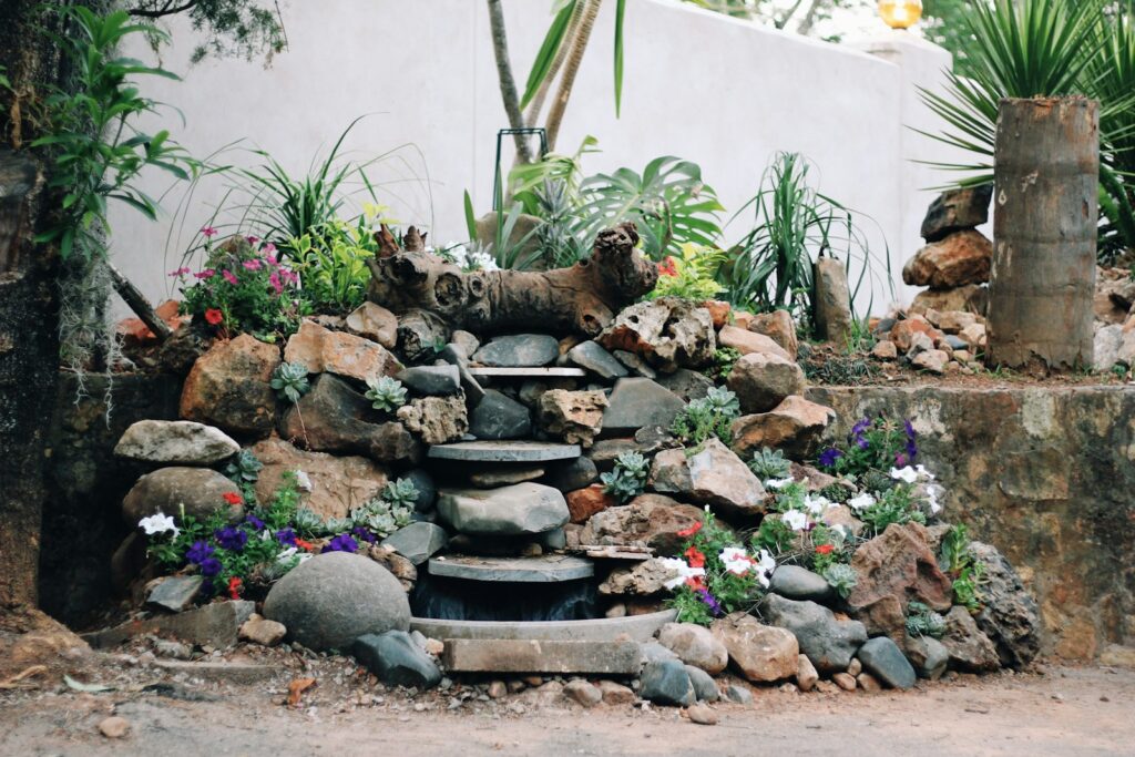 a fountain surrounded by rocks and flowers in a garden
