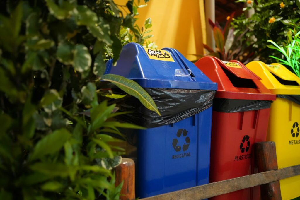 Colorful recycling bins with green foliage.