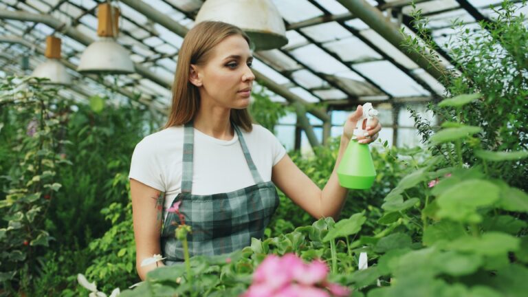 Woman watering plants in a greenhouse.