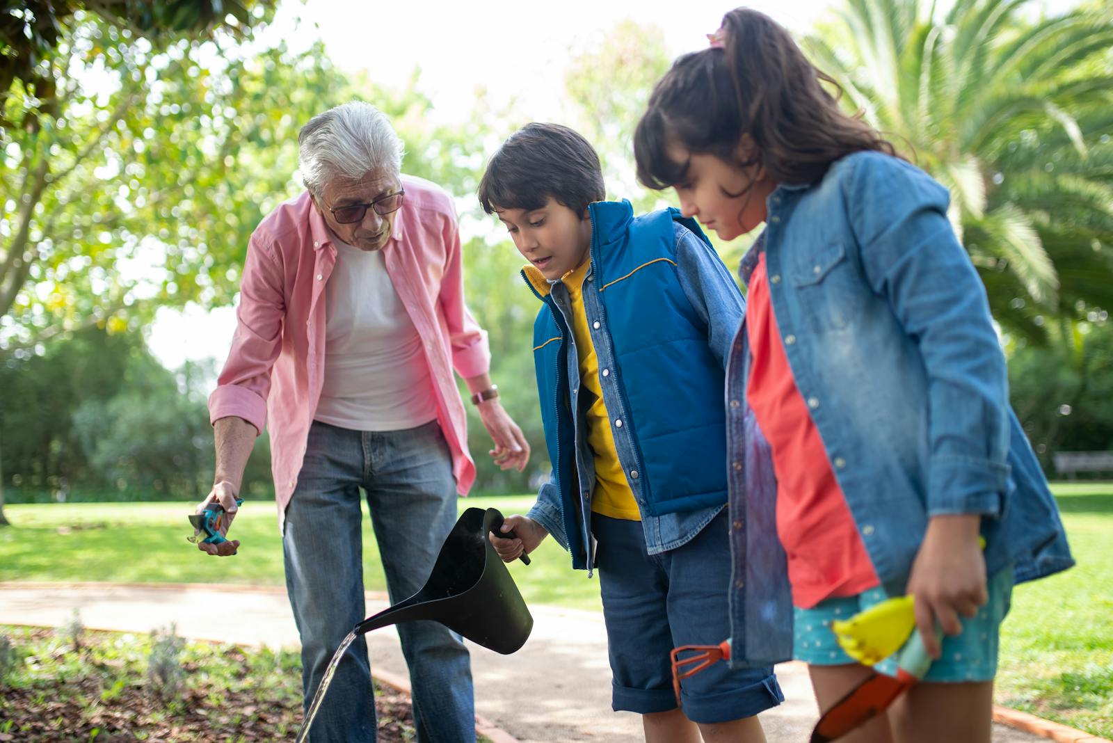 Elderly man gardening with his grandchildren in a sunny park.