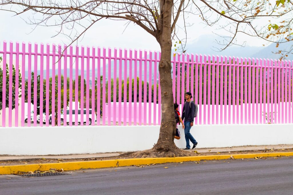 a man walking down a street past a pink fence