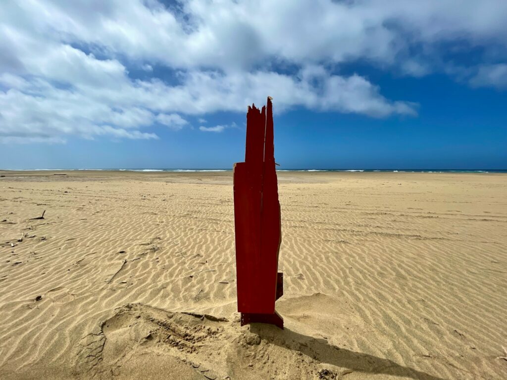 a red piece of art sitting on top of a sandy beach