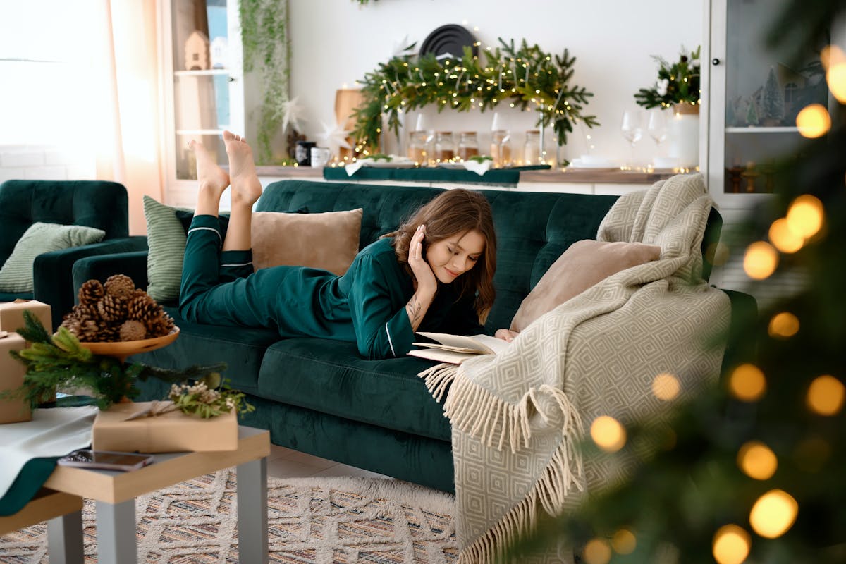 Woman relaxing and reading on a sofa in a Christmas-themed living room with festive decor.