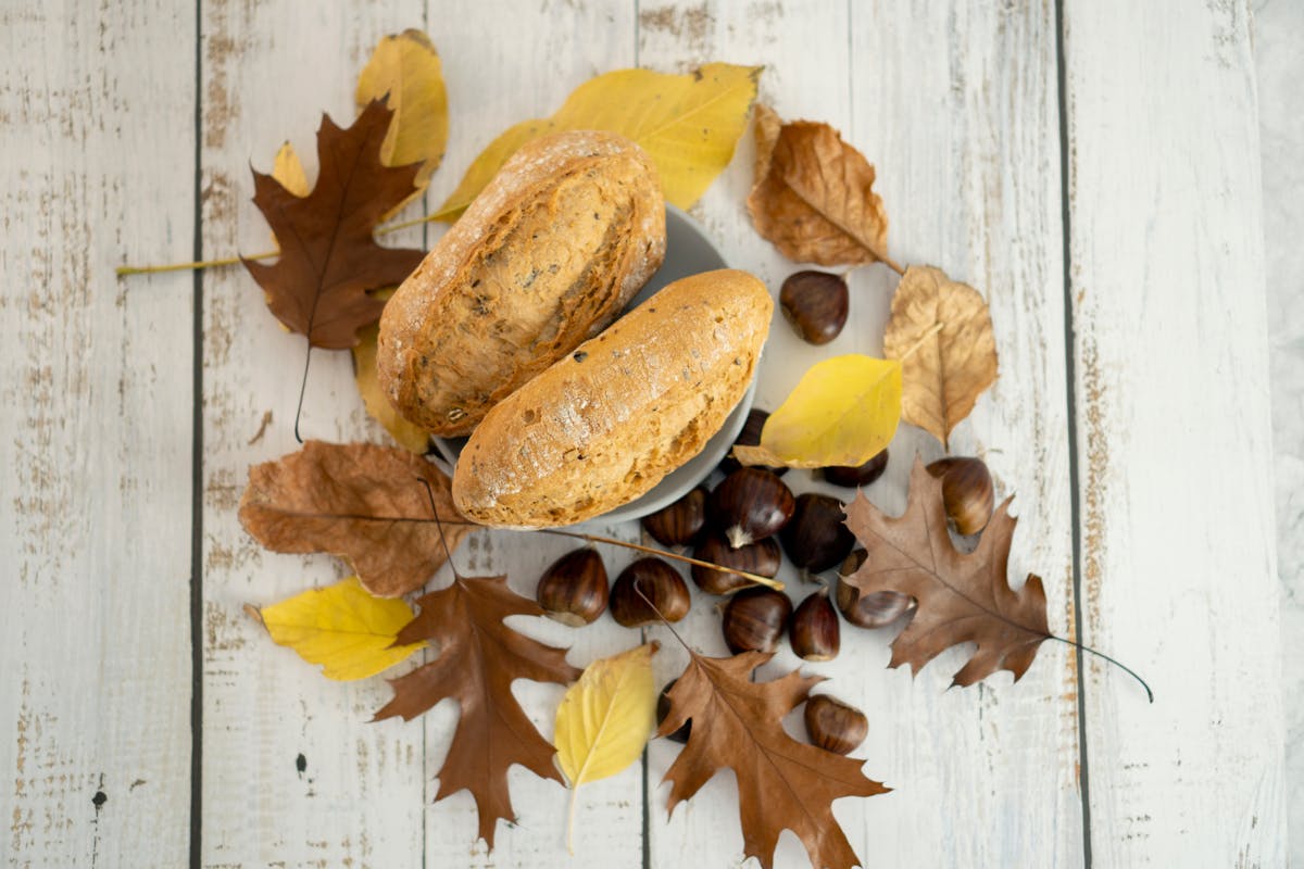 A cozy autumn scene with freshly baked bread, chestnuts, and colorful leaves on a rustic wood table.