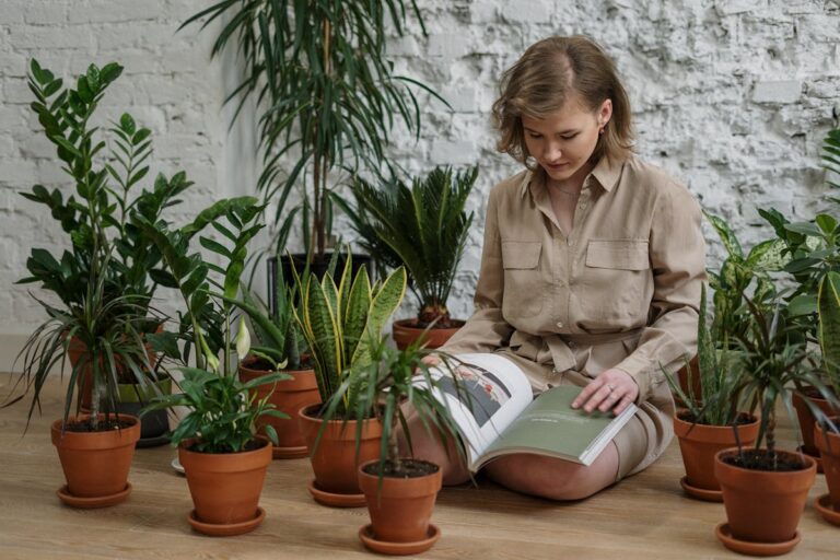 A woman sitting on the floor reading, surrounded by diverse indoor plants.