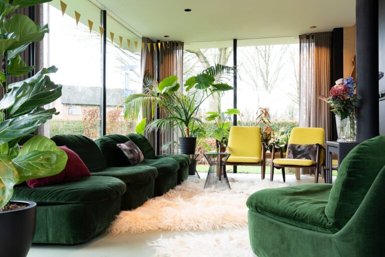 A modern living room featuring a green sofa, yellow chairs, and lush indoor plants, bathed in natural light.