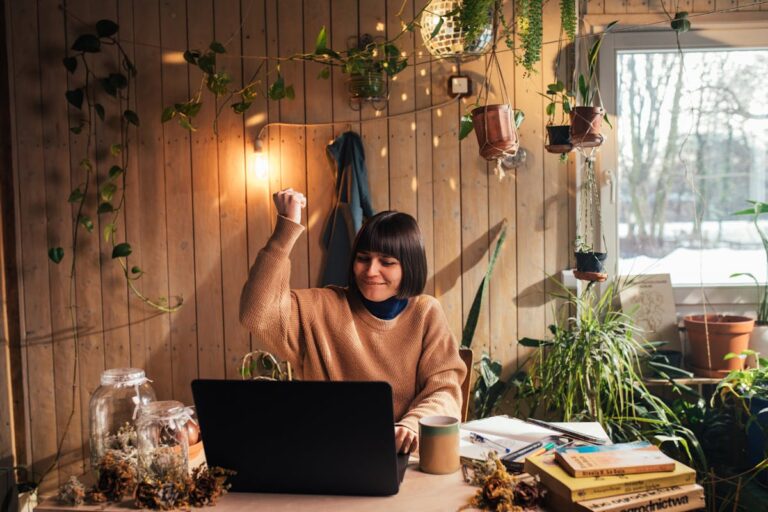 Cheerful woman celebrating a successful moment with her laptop in a cozy home garden environment.