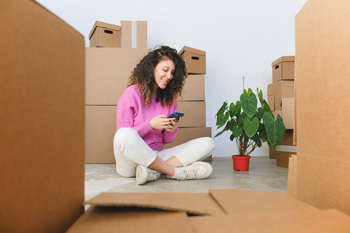 Cheerful woman checking phone surrounded by moving boxes indoors.