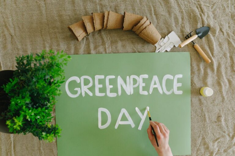 Top view of a hand painting Greenpeace Day on a green poster with gardening tools and plants.